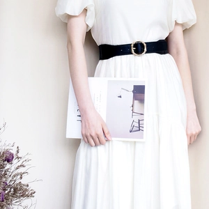 Detail of a wide black elastic belt featuring a golden bamboo texture buckle on a white dress