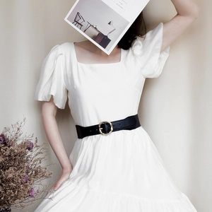 Women's wide black leather belt with round gold buckle on white dress and beige background