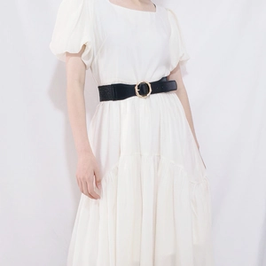 Detail of a wide black elastic waist belt with a golden bamboo-style buckle on a white dress