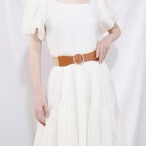 Detail of tan leather waist belt with straw texture and golden round metal buckle on dress