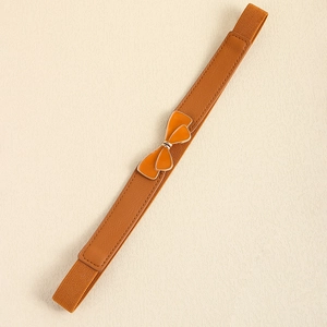 Detail of warm brown elastic skinny belt featuring a glossy orange enamel bow buckle