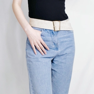 Close-up of beige woven elastic belt with a golden square buckle worn on denim jeans