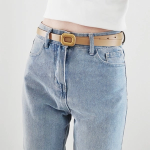 Detail of slim camel brown PU leather belt with matte gold square buckle on blue jeans