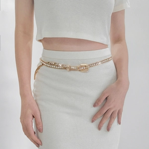 Detail of gold waist chain with rhinestones and horseshoe buckle on white dress