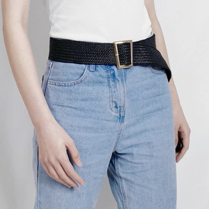 Detail of a wide black woven belt with a gold metal buckle on blue jeans for women