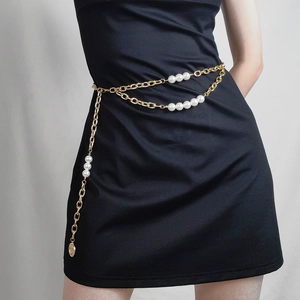 Détail d'une chaîne de taille dorée à deux rangs avec perles et breloque pièce sur robe