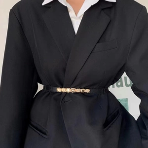 Détail d'une fine ceinture élastique noire avec boucle dorée sur un blazer noir élégant