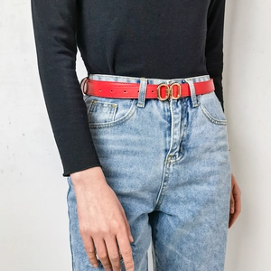 Détail d'une fine ceinture rouge en cuir avec boucle dorée double sur un jean en denim