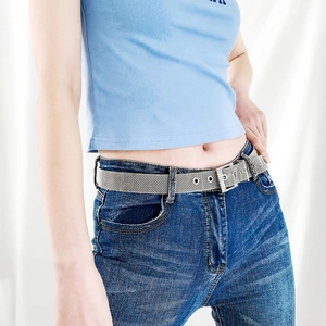 Détail de la ceinture en maille argentée à œillets portée sur un jean bleu et un débardeur