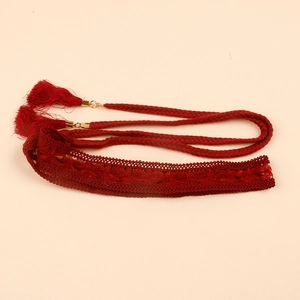 Detailed macro view of dark red braided lace belt with golden metal and bohemian tassels