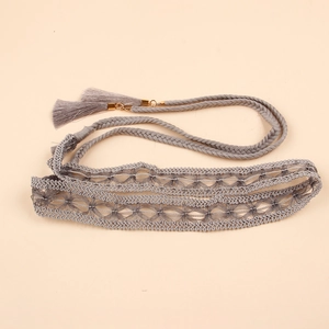 Macro shot of grey braided lace belt with fringe tassels and gold hardware details
