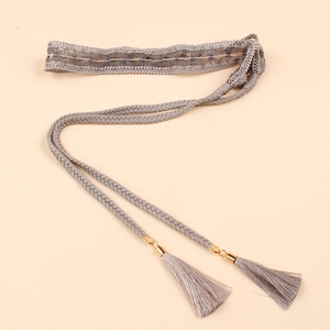 Detail of grey bohemian braided waist belt featuring soft tassels and golden metal accents