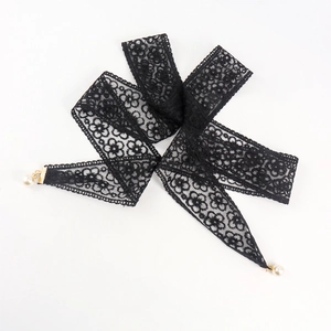 Détail d'une ceinture en dentelle florale noire avec pendentifs perles et fermoirs dorés