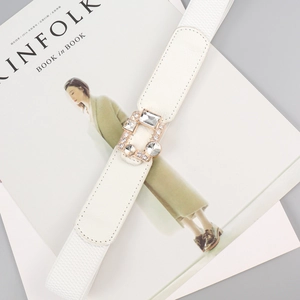 White elastic waist belt with sparkling rhinestone gold buckle on a stylish magazine