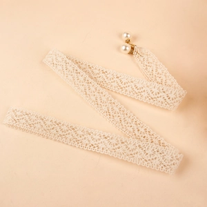 Detalle de cinta de encaje beige con cierre dorado y elegantes colgantes de perlas blancas