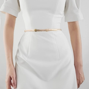 Detail view of a slim gold metal waist belt with woven buckle on a white dress