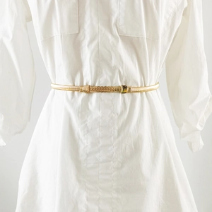 Detail of a thin gold metal elastic waist chain belt with a textured rectangular buckle