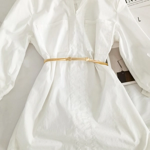 Close-up of golden textured chain belt with metal clasp on a white dress