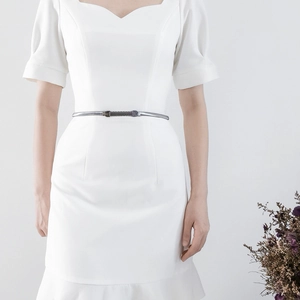 Detail of a thin silver metal belt with wave chain and capsule buckle on a white dress