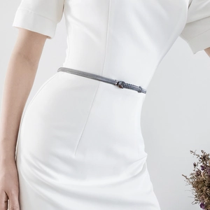 Detail view of a slim gunmetal wave chain belt with spring buckle on a white dress