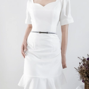Close-up of a stylish silver metal chain belt with capsule buckle on a white dress