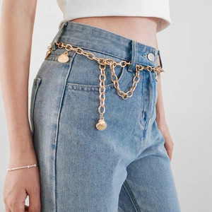 Dettaglio della catena dorata in vita con ciondoli a conchiglia su jeans in denim blu