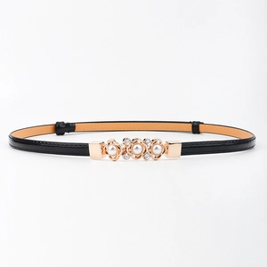 Détail d'une fine ceinture en cuir noir avec boucle dorée ornée de perles et strass