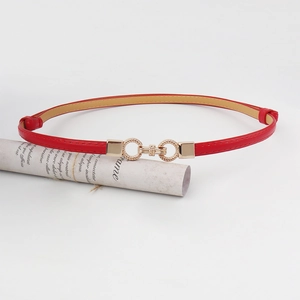 Detailed macro of a thin red faux leather fashion belt with a wavy gold metal buckle