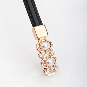 Détail de la boucle fleur dorée avec perles et strass sur la ceinture en cuir verni