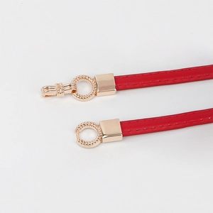 Detail of red leather belt featuring a decorative gold twisted ring buckle and neat stitching