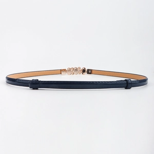 Détail de la ceinture fine en cuir verni bleu marine avec boucle décorative dorée