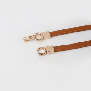 Detail of slim brown leather belt with gold twisted ring buckle and spring hook clasp