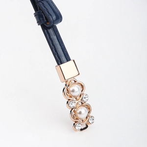 Détail d'une ceinture en cuir verni bleu marine avec boucle dorée, perles et strass