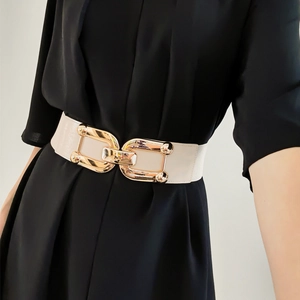 Detail of a chic cream elastic waist belt with a golden metal buckle on black dress