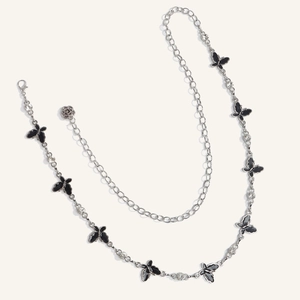 Detail of silver waist chain with black butterfly charms and rose pendant on white background