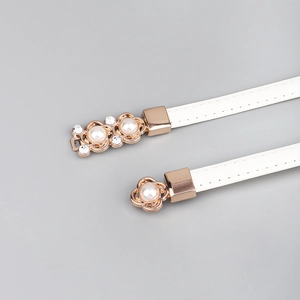 Détail d'une boucle dorée élégante avec perles et strass sur une ceinture fine en cuir blanc
