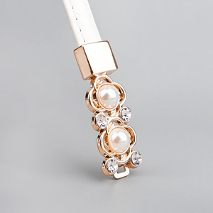 Détail de boucle or rose avec perles et cristaux sur une fine ceinture en cuir blanc