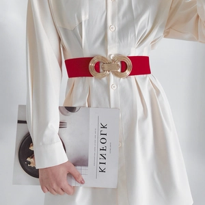 Detail of red elastic waist belt with a golden geometric metal buckle on a white dress