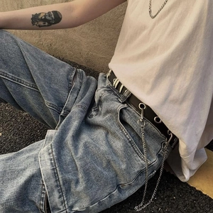 Detail of a punk style black metal eyelet belt with a silver hanging long chain on jeans