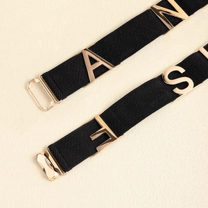 Close-up of black elastic belt featuring polished gold metal letters and hardware