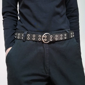 Detail of punk style black double-grommet belt with silver twin-pin buckle on trousers
