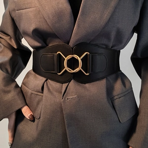 Detail of a black wide elastic waist belt with a gold geometric metal buckle on a blazer