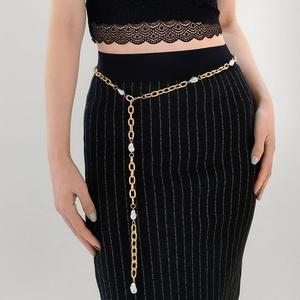 Detail eines eleganten Goldketten-Taillengürtels mit weißen Perlen an einem schwarzen Kleid