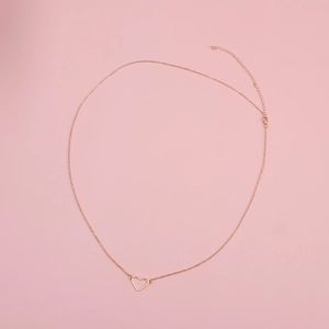 Dettaglio del ciondolo a cuore in oro rosa su una catena sottile su sfondo rosa