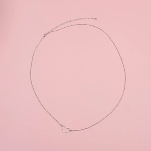 Dettaglio macro di una catena con pendente a cuore argento su sfondo rosa per spiaggia