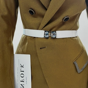 Détail d'une ceinture élastique blanche avec boucle cristal sur un blazer jaune