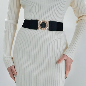 Détail d'une ceinture élastique noire avec boucle ronde dorée sur une robe blanche