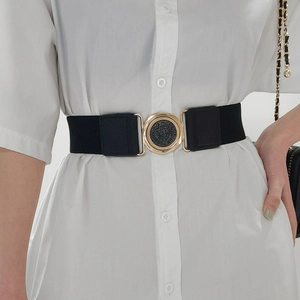 Détail d'une ceinture élastique noire avec boucle ronde dorée sur une robe blanche