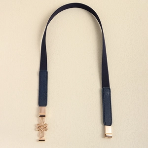 Detail of navy elastic belt featuring a golden knot buckle and textured leather tips