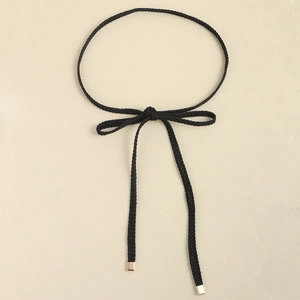 Detail of black woven thin belt with gold square metal tips and an elegant bow knot